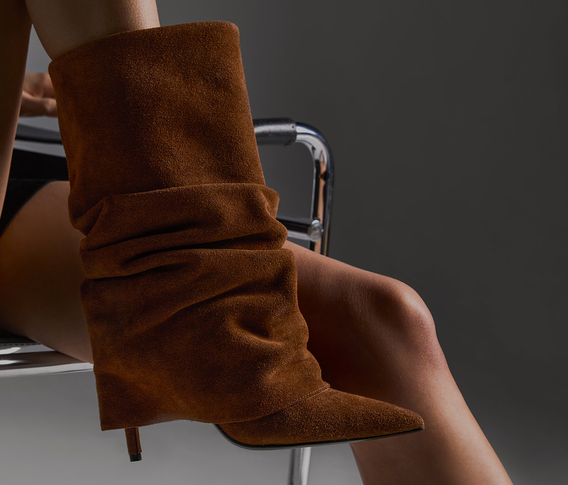 A person wearing a brown suede slouchy boot with a high heel, showcasing a modern, updated classic silhouette.
