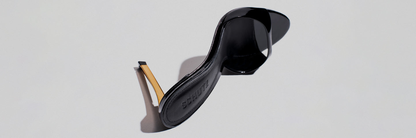 Elegant black patent mule sandal featuring a glossy finish, open toe, and a thin metallic gold heel, placed on a light neutral background.