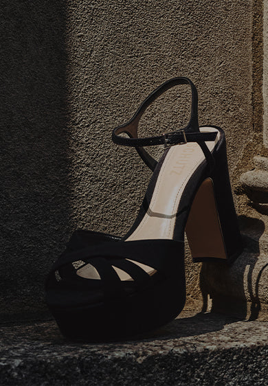 Women’s black platform sandals with a chunky block heel, styled against a stone architectural background with dramatic lighting.