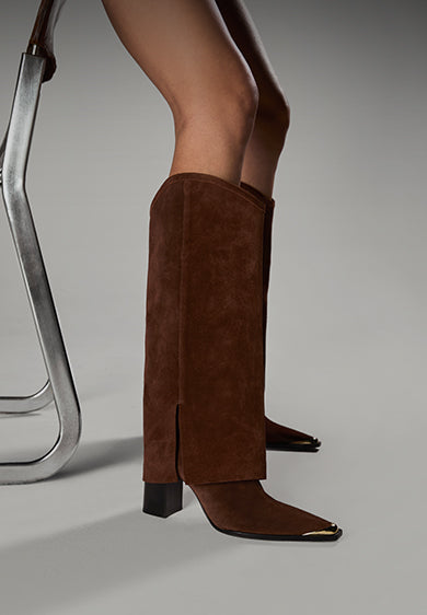 Close-up of brown suede knee-high boots with gold-tipped toes, styled next to a metal chair.