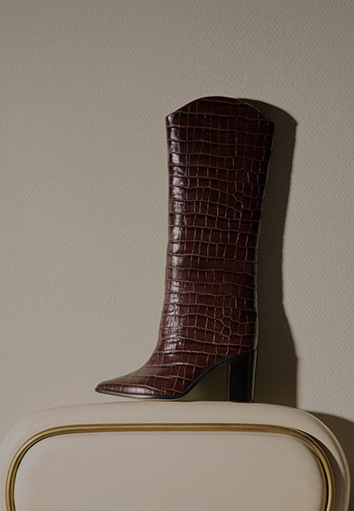 Promotional banner featuring a brown crocodile-embossed knee-high boot with a block heel against a neutral background, with the text ‘Best Sellers’ and a subtitle highlighting bestselling shoe style