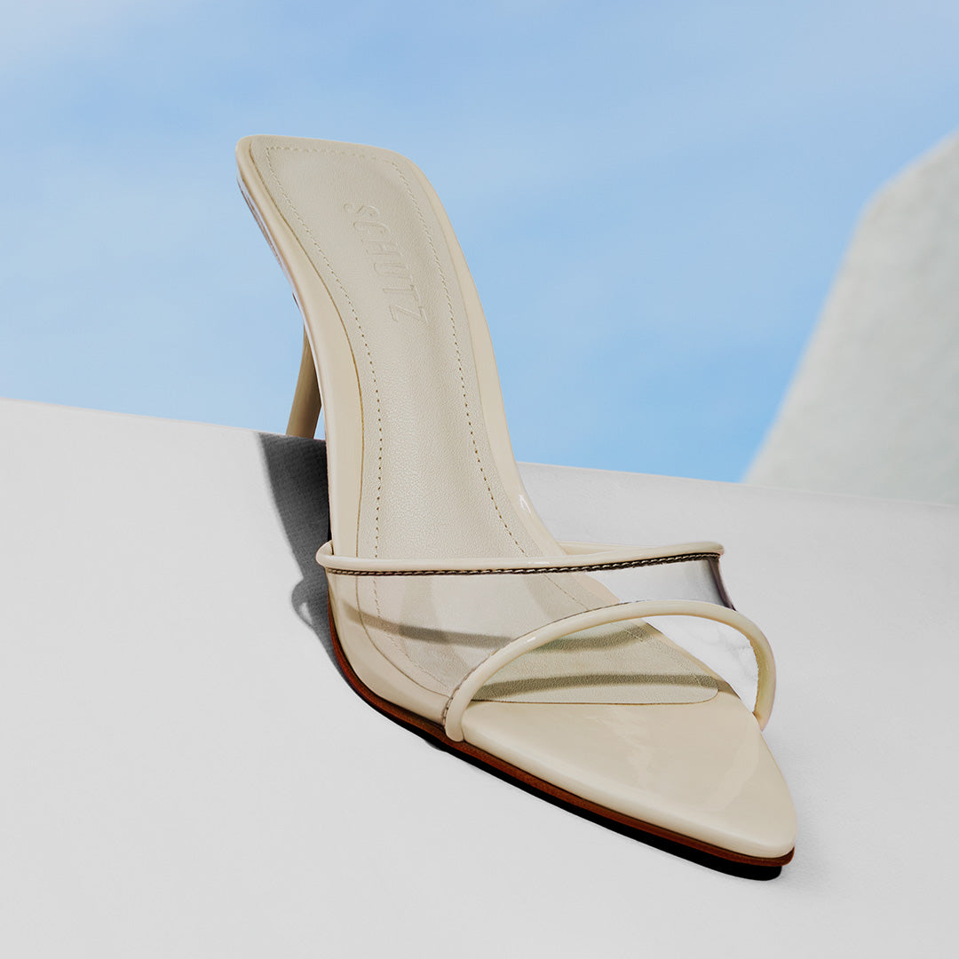 Cream pointed-toe heeled sandal with transparent strap displayed against a blue background.