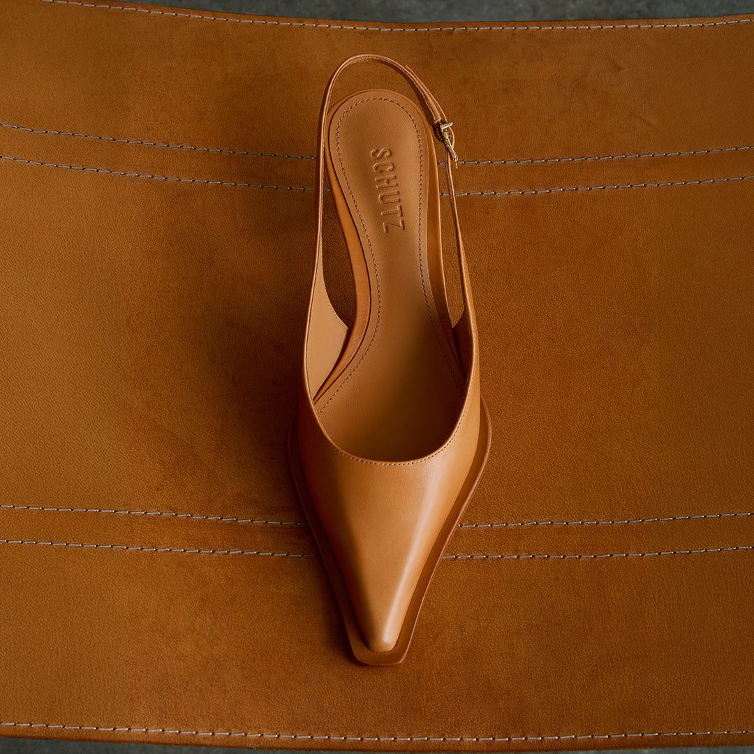 Beige pointed-toe high heel displayed on a matching leather surface, highlighting its elegant design and high-quality finish.