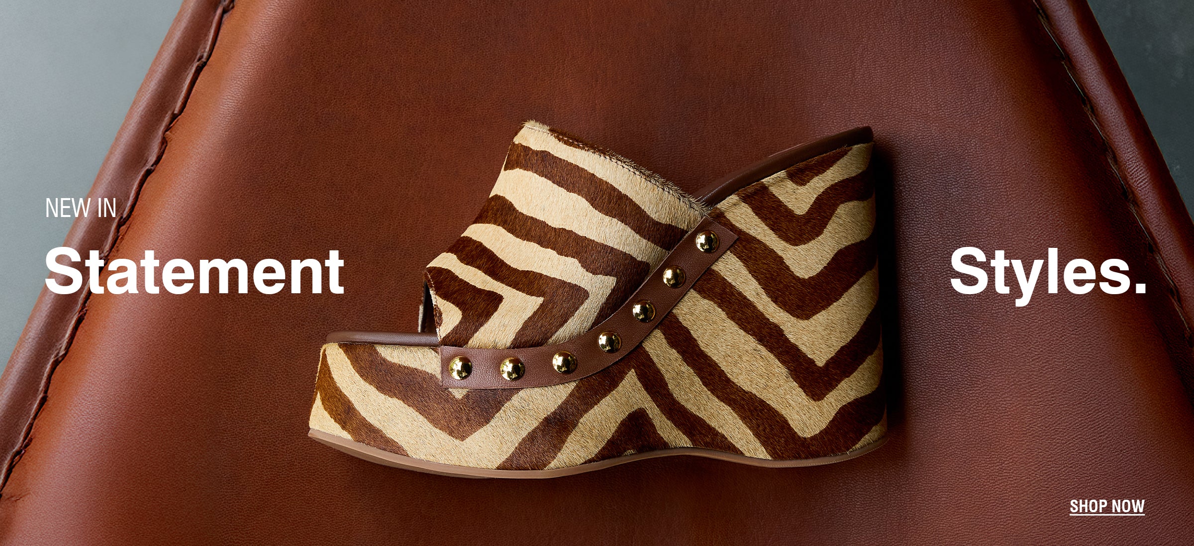 Zebra-patterned wedge shoe with stud details on a leather surface. Bold text reads "New in Statement Styles." Minimalist, fashionable tone.
