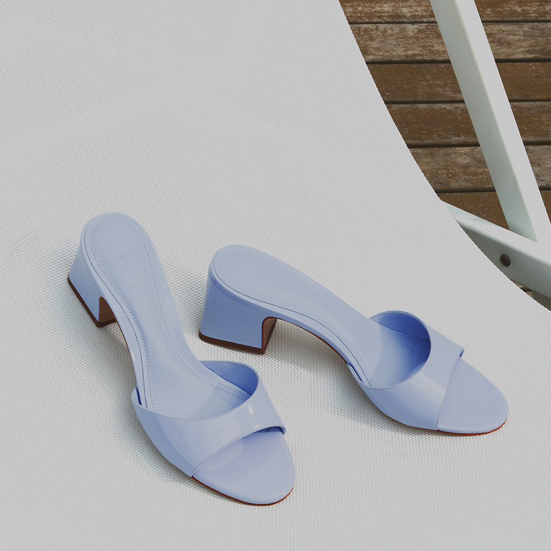 Light blue heeled sandals on a white textured lounge chair, placed outdoors on a wooden deck. The scene conveys a summery, relaxed vibe.