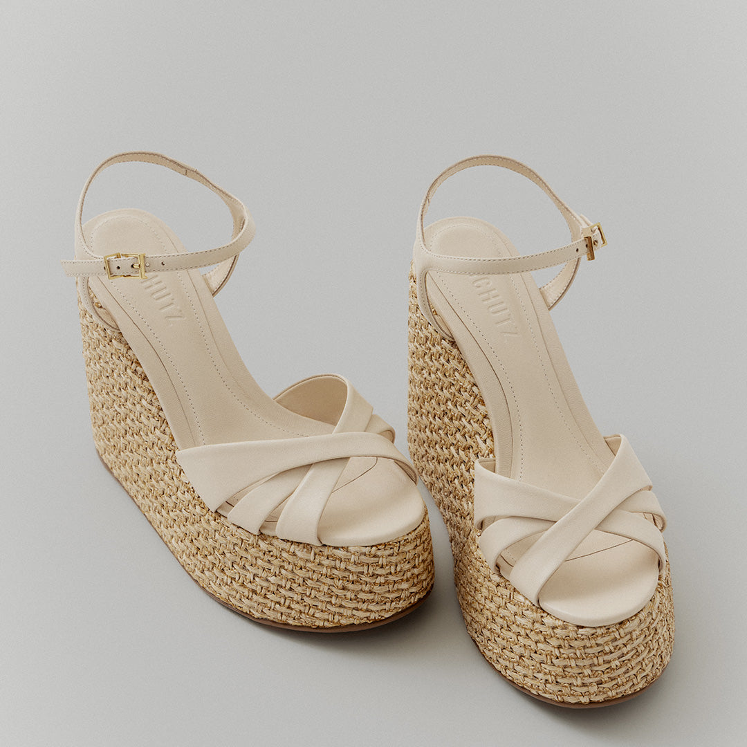 Beige wedge sandals with crisscross straps and ankle buckles. The platform is made of woven straw, creating a casual, summery look.