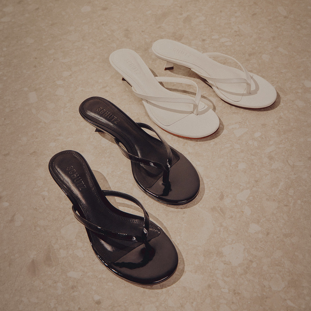 Two pairs of heeled sandals on a marble floor; one pair is white, andthe other is black, with a glossy finish, evoking elegance and simplicity.