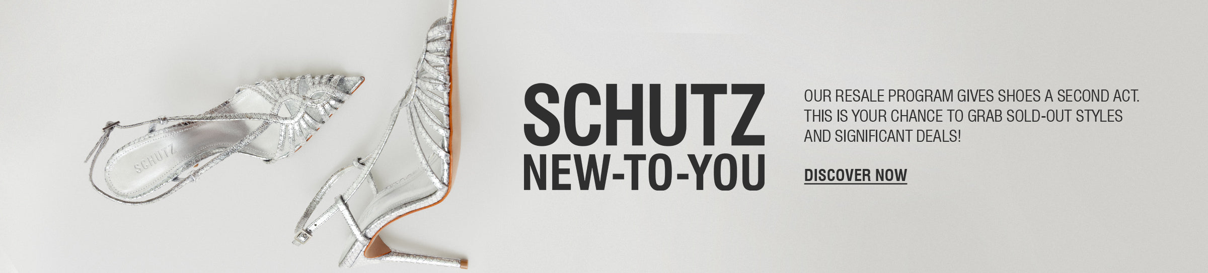 A person's legs and feet are visible on a crosswalk. They are wearing a pair of silver metallic high-heel mules with two thin straps over the foot. The text "SCHUTZ NEW-TO-YOU" and "DISCOVER NOW" are on the right side of the image, advertising a resale program.