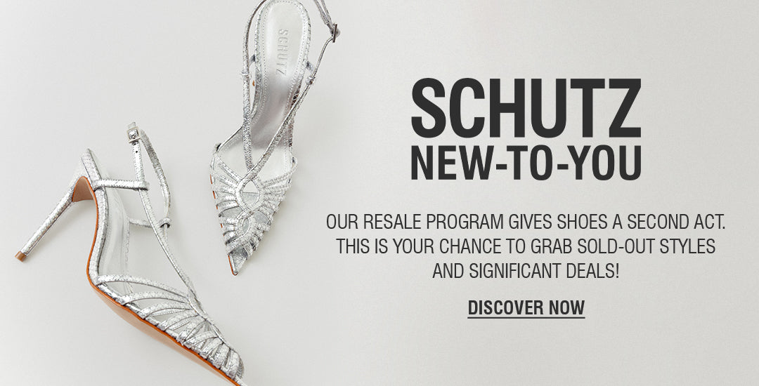 A person's legs and feet are visible on a crosswalk. They are wearing a pair of silver metallic high-heel mules with two thin straps over the foot. The text "SCHUTZ NEW-TO-YOU" and "DISCOVER NOW" are on the right side of the image, advertising a resale program.