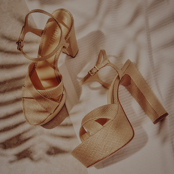 Golden high-heeled sandals with textured straps on a soft surface. Warm lighting casts elegant shadow patterns, creating a stylish, sophisticated mood.