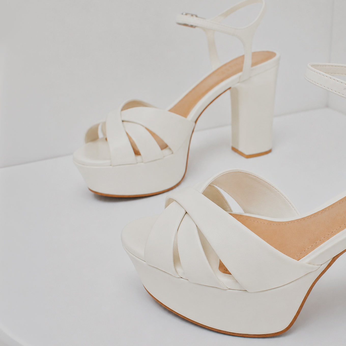 White platform sandals with crisscross front straps, ankle strap and block heel displayed on a white surface.