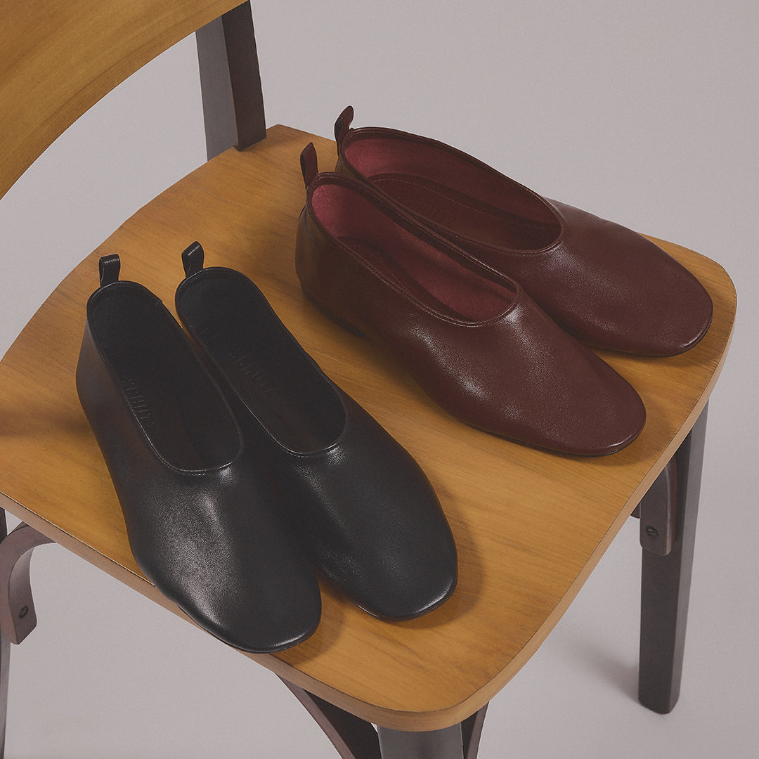 Black and burgundy leather ballet flats displayed on a wooden chair.
