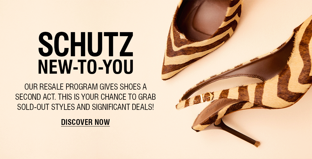 A person's legs and feet are visible on a crosswalk. They are wearing a pair of silver metallic high-heel mules with two thin straps over the foot. The text "SCHUTZ NEW-TO-YOU" and "DISCOVER NOW" are on the right side of the image, advertising a resale program.