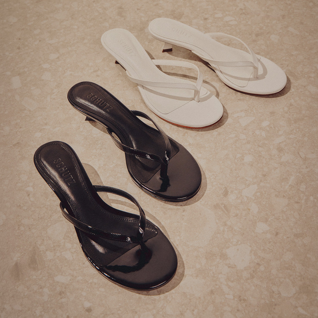 Two pairs of black and white sandals displayed on a polished marble floor.