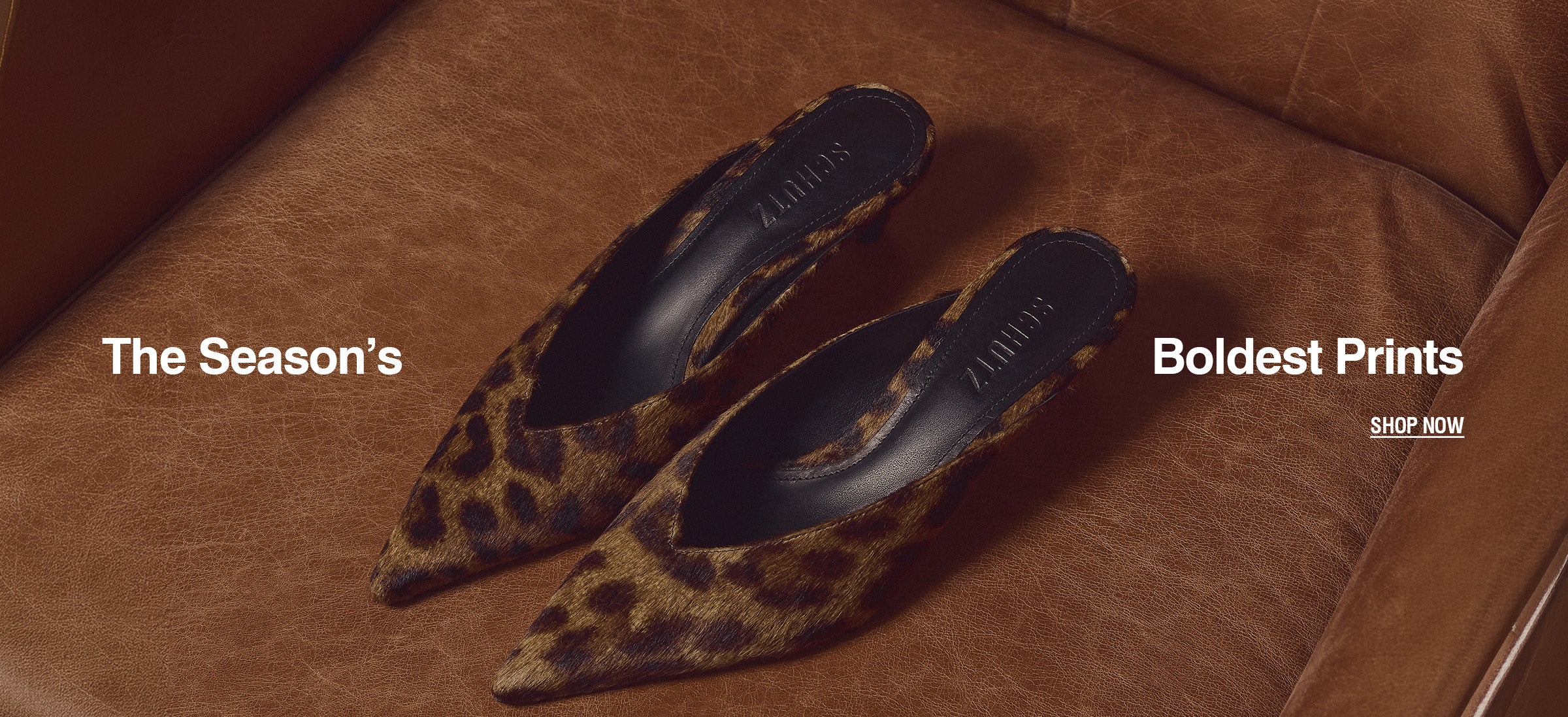 Leopard print pointed-toe mules with SCHUTZ insoles rest on a brown leather chair. Text Reads: The Season’s Boldest Prints. Shop Now.
