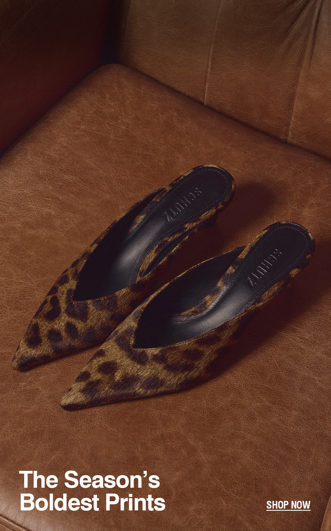 Leopard print pointed-toe mules with SCHUTZ insoles rest on a brown leather chair. Text Reads: The Season’s Boldest Prints. Shop Now.