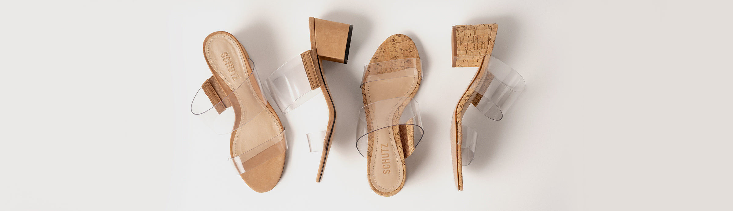 Four women's heeled sandals arranged on a clean off-white background. The sandals feature clear transparent straps, tan leather uppers, and cork-look heel blocks.