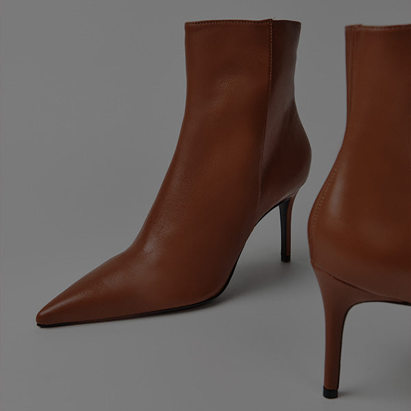 A pair of brown leather ankle boots with pointed toes and slim high heels, shown on a neutral gray background.