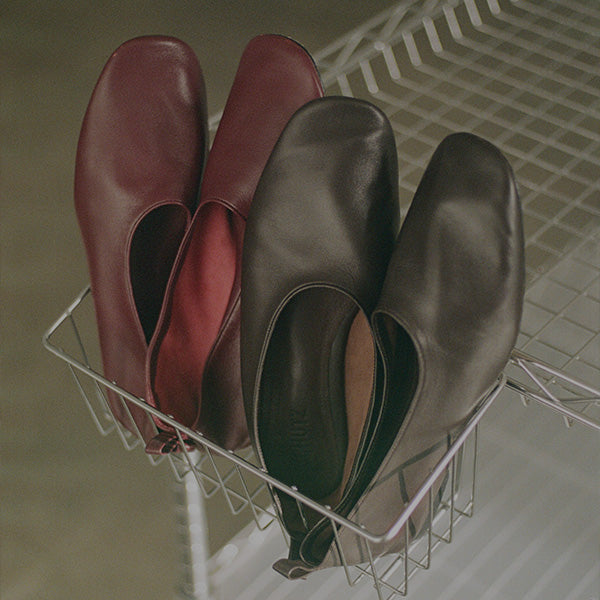 Two pairs of leather slip-on flats in burgundy and dark brown, displayed in a wire basket.