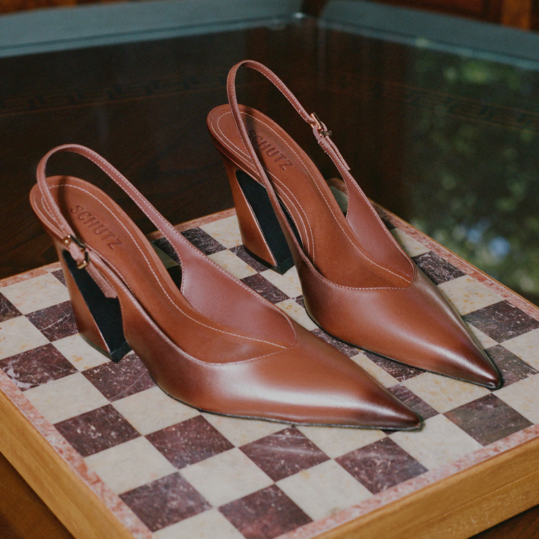 A pair of brown leather slingback pointed-toe high heels with block heels, displayed on a checkered marble tray.