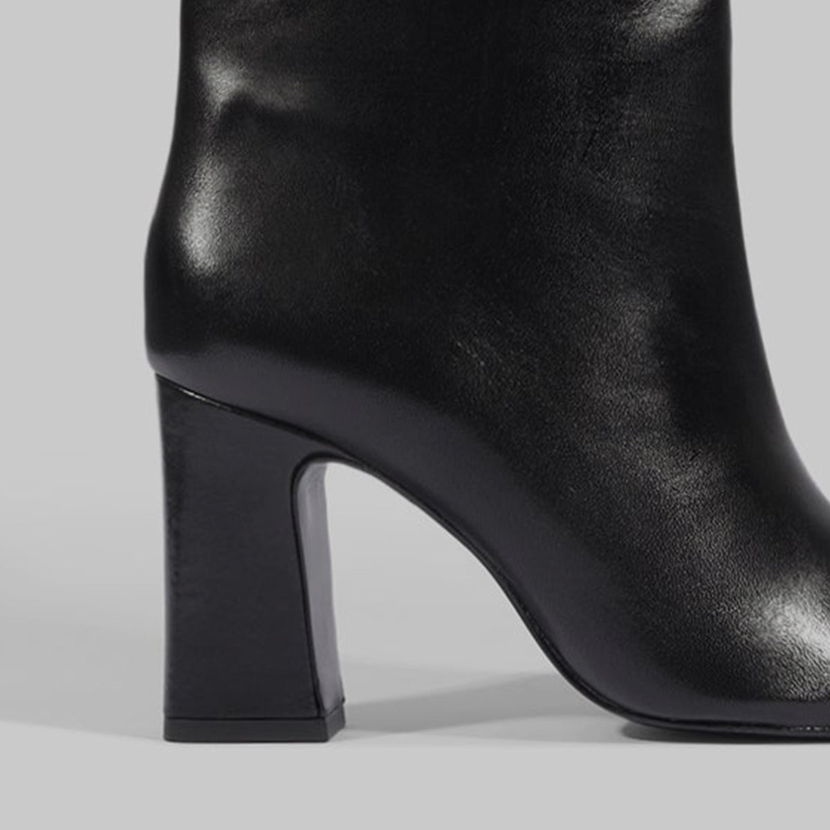 Close-up of a black leather ankle boot with a chunky block heel, shown from the side against a light gray background.
