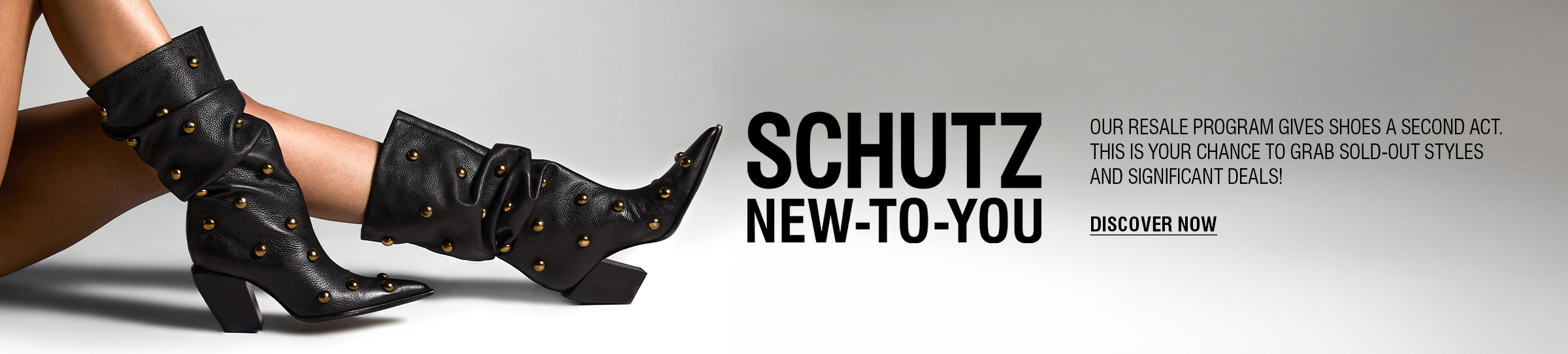 A person's legs and feet are visible on a crosswalk. They are wearing a pair of silver metallic high-heel mules with two thin straps over the foot. The text "SCHUTZ NEW-TO-YOU" and "DISCOVER NOW" are on the right side of the image, advertising a resale program.