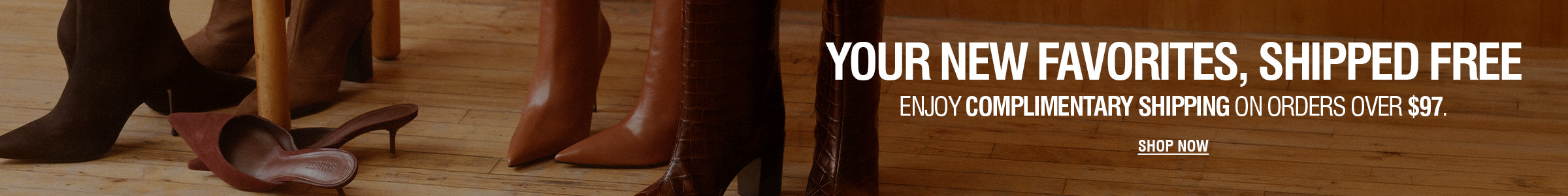 Promotional banner with large white text reading 'YOUR NEW FAVORITES, SHIPPED FREE' over a warm brown interior scene showing shoes and boots on a wooden floor, plus 'ENJOY COMPLIMENTARY SHIPPING ON ORDERS OVER $97' and a 'SHOP NOW' button.