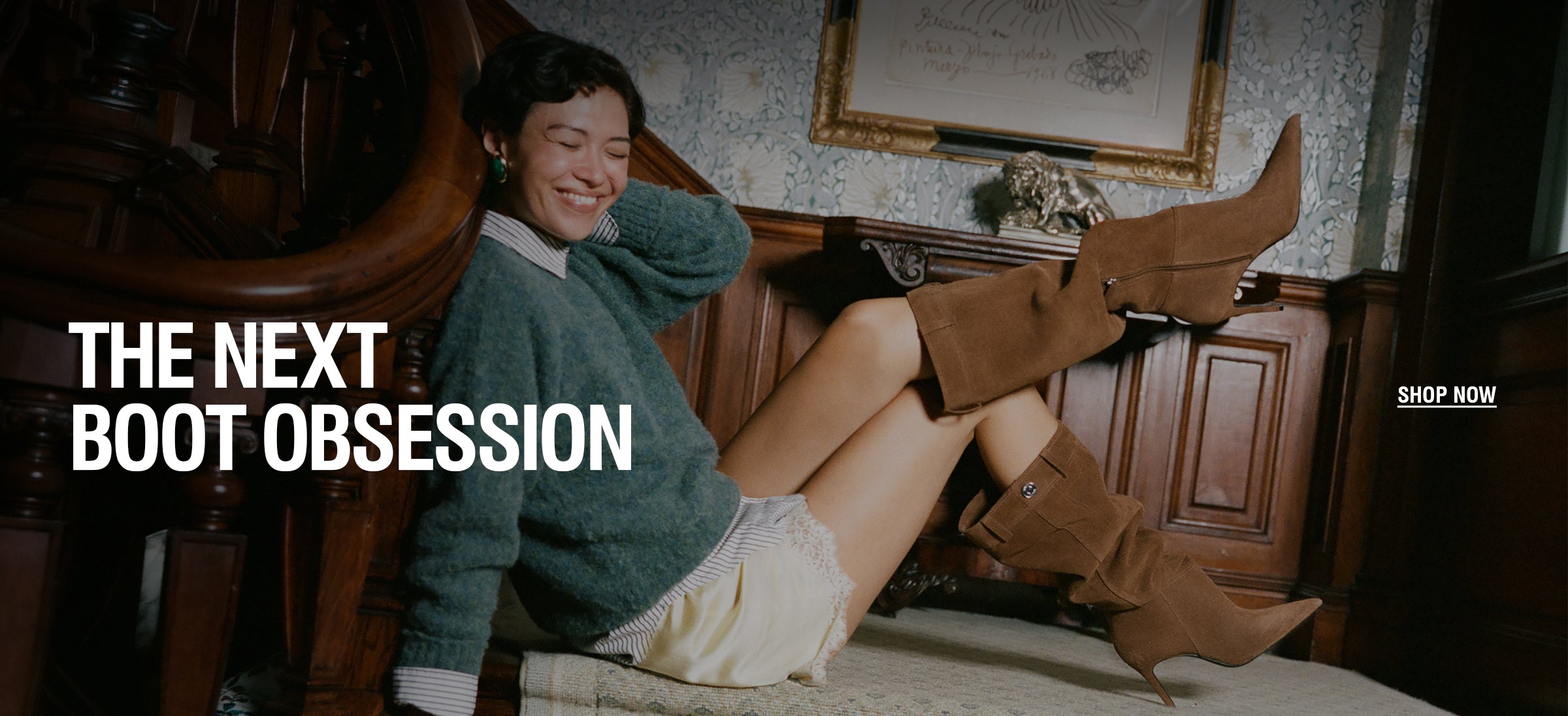 A woman sits on a patterned carpeted staircase in a vintage room, wearing a teal knit sweater, a striped collared shirt, and brown suede knee-high boots. Large white text on the left reads 'THE NEXT BOOT OBSESSION' with 'SHOP NOW' below.