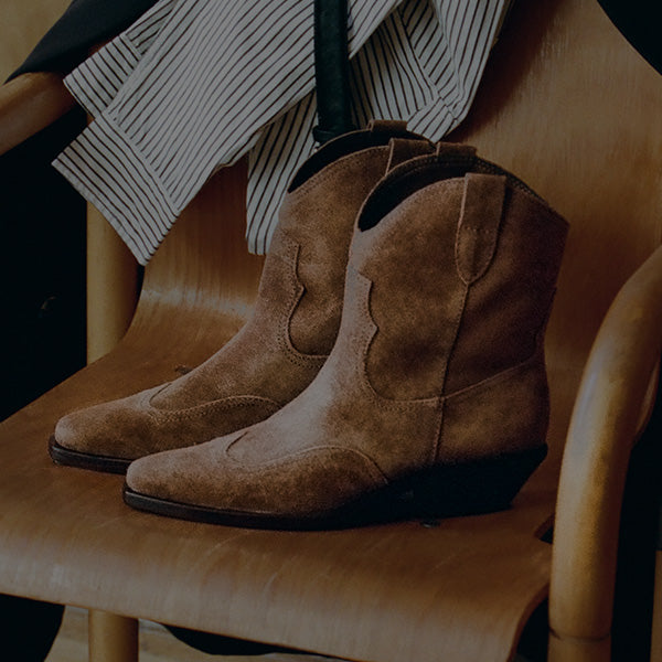 Pair of brown suede western ankle boots resting on a wooden chair.