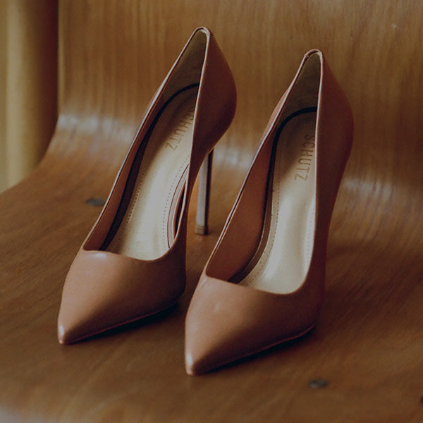 Pair of classic nude leather pointed-toe high-heeled pumps on a wooden chair.