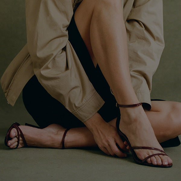 Person sitting cross-legged wearing dark burgundy strappy high-heeled sandals.