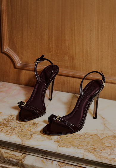 Pair of dark glossy high-heeled sandals with thin straps displayed on a marble surface, with the text ‘WOMEN’S SANDALS’ on the left