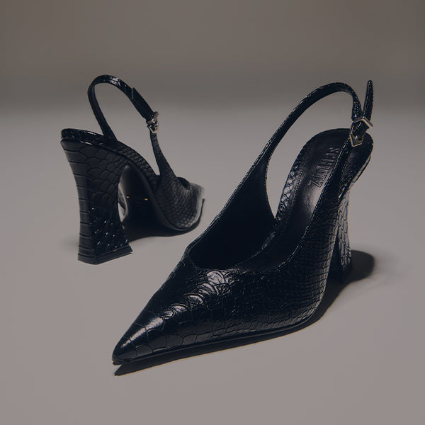Overhead shot of two black leather slingback pumps with a deep V-cut vamp, a square toe, and a striking wedge heel, resting on a gray background.
