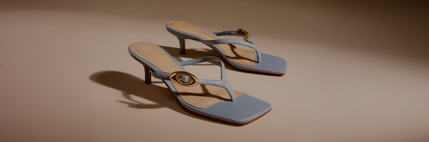 Promotional banner featuring a pair of light blue mid-heel sandals with square toes and gold ring details, set against a neutral background, with the text ‘Mid Heel Sandals’ and a subtitle describing their versatility from work to play.