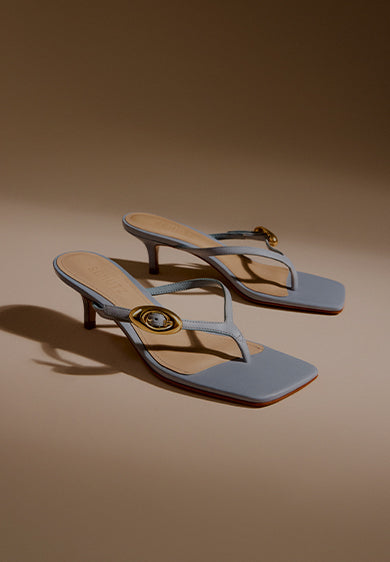Promotional banner featuring a pair of light blue mid-heel sandals with square toes and gold ring details, set against a neutral background, with the text ‘Mid Heel Sandals’ and a subtitle describing their versatility from work to play.
