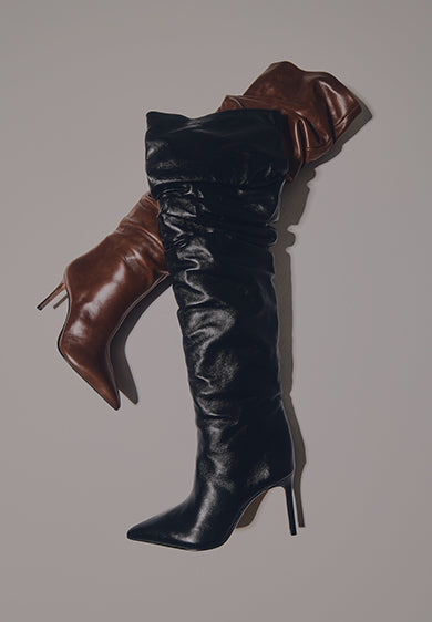 A pair of high-heeled, over-the-knee slouch boots. One boot is brown and the other is black, crossing over each other. The word BOOTS is written in large white letters on the left side of a plain gray background.