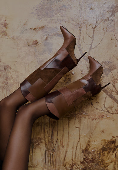 Fashion editorial image of a woman wearing high-heeled boots in rich brown tones, styled for an evening look against a textured background.