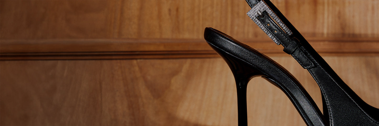 Black stiletto slingback heel with a decorative buckle, displayed against a wooden background