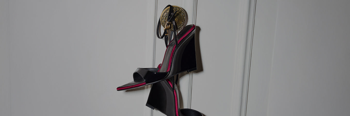 A pair of black platform wedge sandals with pink trim hanging by their straps from a decorative wall hook
