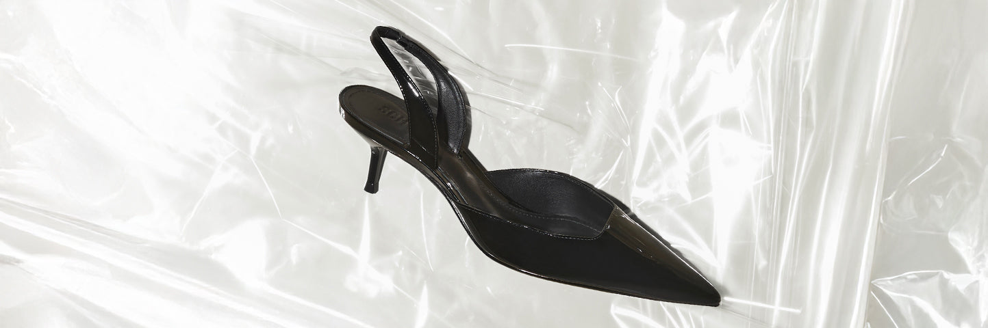 Black pointed-toe slingback pumps with stiletto heel, placed on a translucent surface.