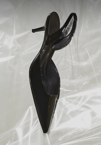 Black pointed-toe slingback pumps with stiletto heel, placed on a translucent surface.