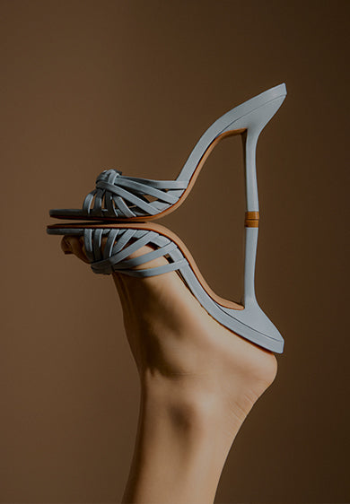 Promotional banner featuring a light blue stiletto sandal with slim straps and a high heel, shown in close-up against a warm gradient background, with the text ‘Stiletto Sandals’ and a subtitle about versatile day-to-night styling.