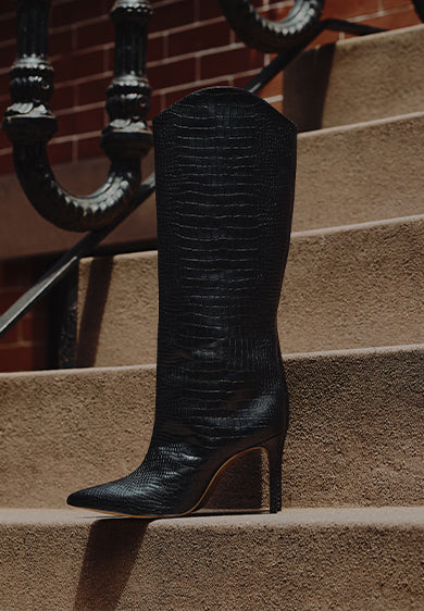 Women’s black knee-high boots with a structured block heel, styled on stone steps in an urban outdoor setting.