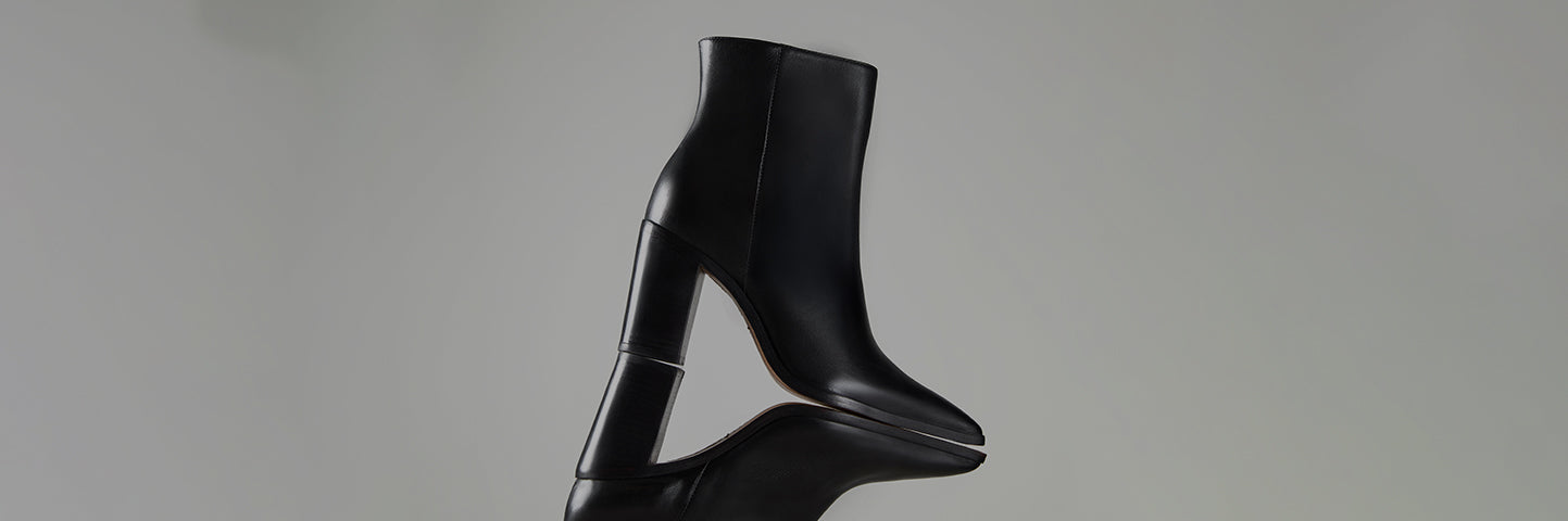 Women’s black ankle boots with a high heel and smooth leather finish, photographed against a neutral background with a mirrored reflection.