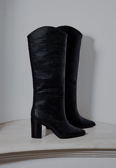 A pair of tall black textured Maryana boots standing upright against a light gray wall.