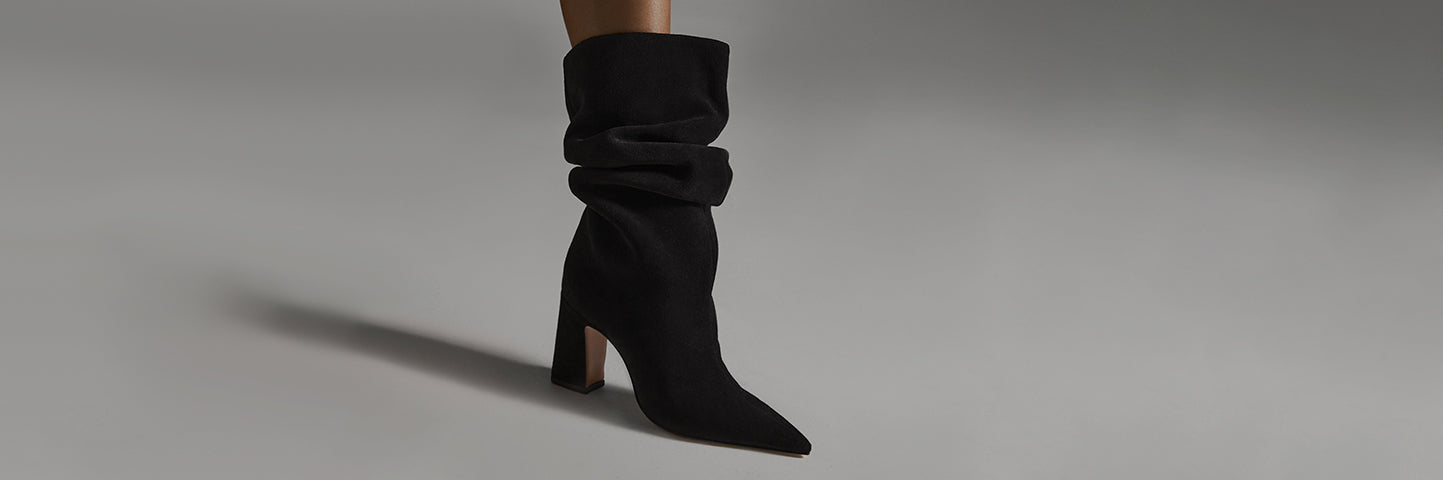 Women’s black heeled boots with a soft slouchy shaft, styled in a minimalist studio scene highlighting silhouette and texture.