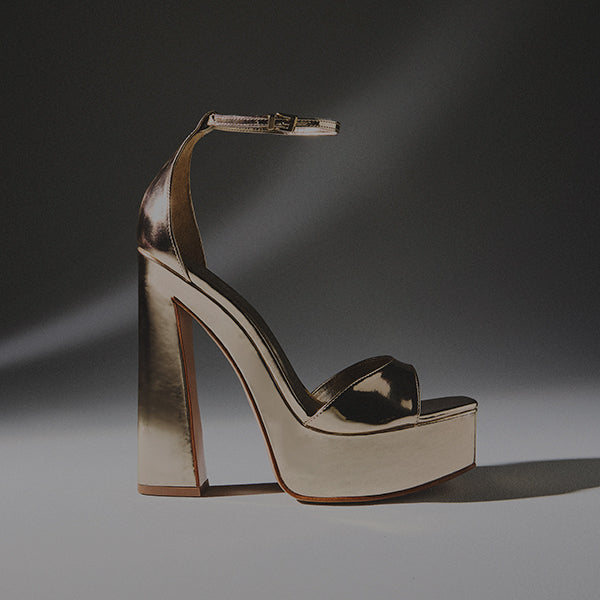 Overhead shot of a pair of black high-heel thong sandals with a pointed toe and thin stiletto heel, photographed against a glossy, wrinkled gray surface.