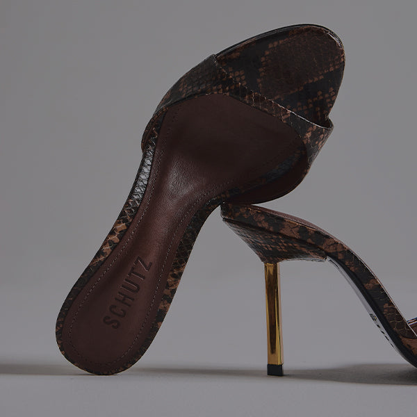 Close-up of a single black patent leather slide mule with a high, thin stiletto heel featuring a gold tone core, viewed from a high angle.