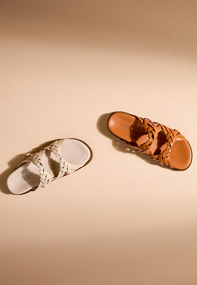 Flat lay of women’s leather sandals in neutral tones arranged on a light background, styled for a relaxed vacation mood.