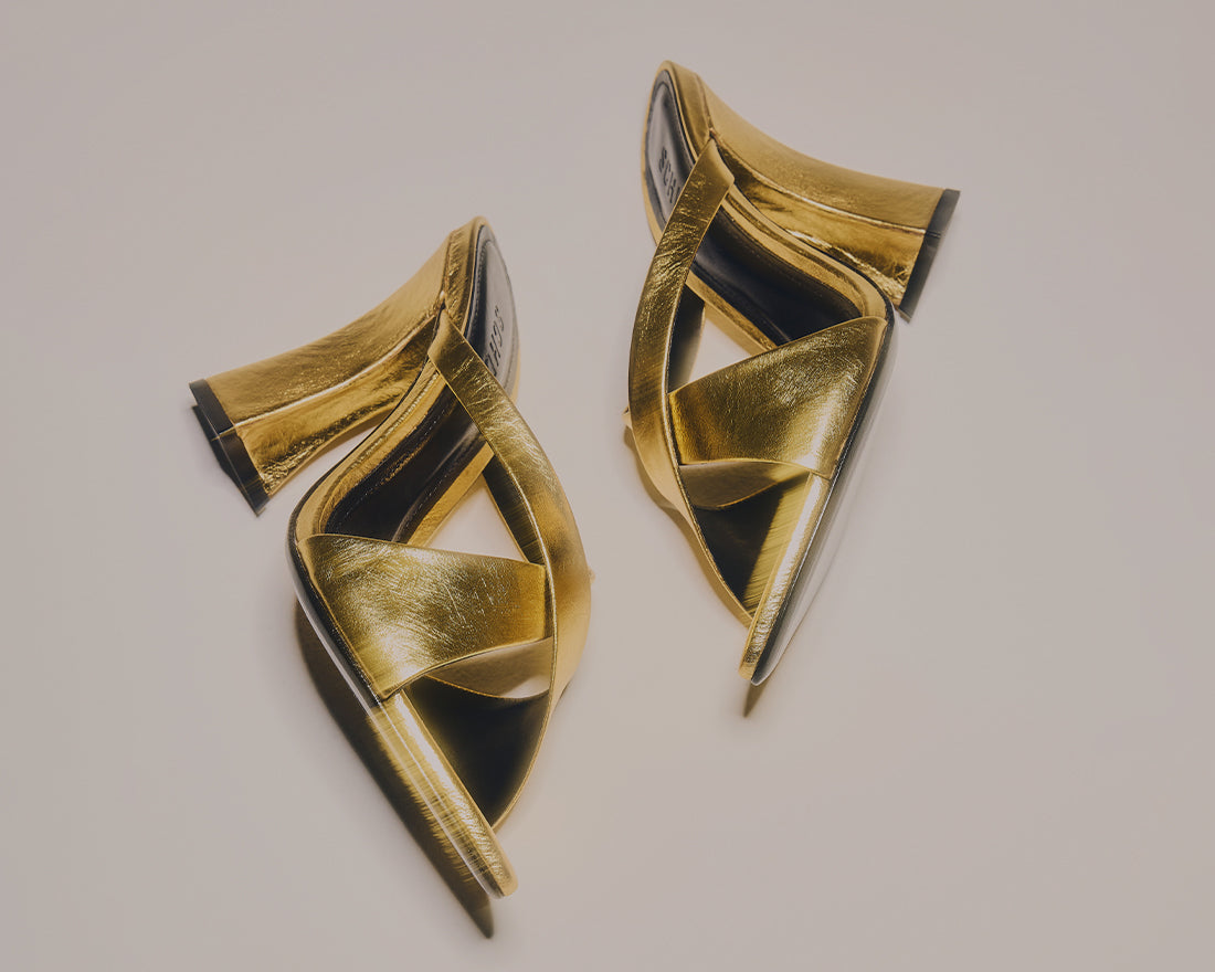 Advertisement for festive wear showing a close-up of a gold high-heeled mule sandal with a sculptural heel. The text overlay reads "FESTIVE NIGHTS" with a "SHOP NOW" button.